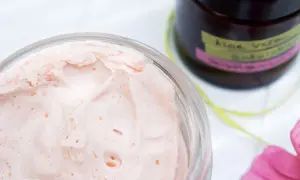 Cremige, rosafarbene Bodylotion mit Sheabutter in einem Glas. Daneben eine Flasche mit "Aloe Vera Bodylotion".