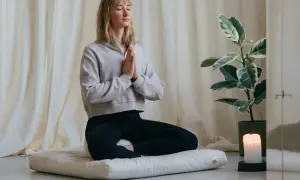 Frau in Meditation, die auf einem Kissen sitzt und mit geschlossenen Augen und gefalteten Händen zur Ruhe kommt. Sie übt, Sorgen loszulassen.