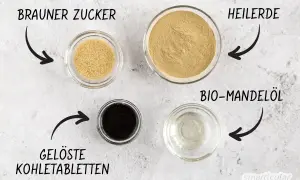Zutaten für eine Maske gegen Pickel selber machen: Brauner Zucker, Heilerde, gelöste Kohletabletten und Bio-Mandelöl.