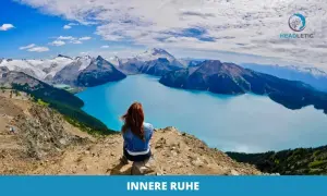 Frau meditiert gegen Angst und innere Unruhe auf einem Berg mit Blick auf einen türkisfarbenen See und schneebedeckte Gipfel.