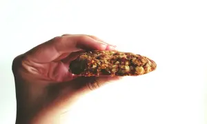 Hand hält ein Haferflocken-Keks. Warum keine Haferflocken bei Fructoseintoleranz? Haferflocken können bei Fructoseintoleranz Probleme bereiten.