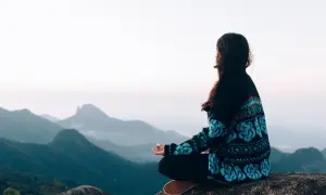 Frau meditiert auf einem Felsen mit Blick auf nebelverhangene Berge. Sie übt schweigen statt reden, um innere Ruhe zu finden.