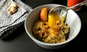 Haferflocken mit Apfelstücken und Rosinen, übergossen mit Honig. Ein leckeres Frühstück, inspiriert von TCM Rezepten. Ingwer liegt daneben.