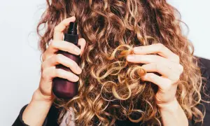 Frau sprüht mit einer Flasche auf ihre lockigen Haare. Perfekt für alle, die ihren eigenen Haarfestiger selber machen wollen.