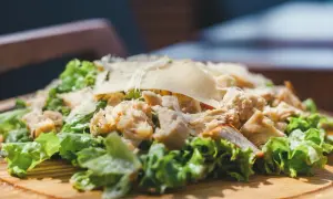 Frischer Romana Salat mit Hähnchenbrust und Parmesan, serviert auf einem Holzbrett.