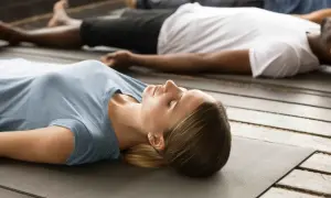 Frauen und Männer liegen entspannt auf Matten und lernen, wie meditiert man im liegen. Sie ruhen sich aus und atmen tief ein.