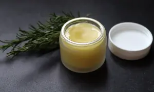 Ein Glas mit selbstgemachter Rosmarinsalbe neben einem Rosmarinzweig. Perfekt zum Rosmarin Salbe selber machen.