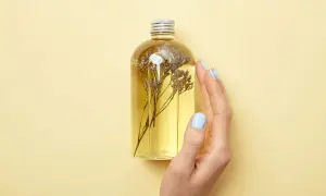 Eine Hand mit hellblauen Nägeln berührt eine Flasche mit gelbem Öl und getrockneten Blumen. Perfekt für duschgel selber machen ohne seife.