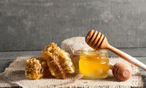 Honigwaben und ein Glas Honig mit einem Honigtaucher. Perfekt, um eine Honigmaske selber zu machen für natürliche Hautpflege.