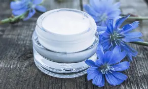 Creme für trockene Haut: Ein Glas mit weißer Creme neben blauen Wegwartenblüten auf Holz. Perfekt zum gesichtscreme selber machen trockene haut.