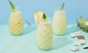 Erfrischende Kokoswasser Rezepte: cremige Drinks in Ananas-Gläsern, garniert mit Ananasblatt und Kokosstückchen.