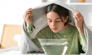 Junge Frau genießt nach dem Dampfbad das Gesicht waschen. Der warme Dampf öffnet die Poren und reinigt die Haut.