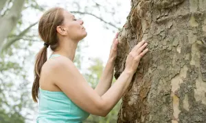 Frau umarmt einen Baum, um achtsam zu sein und die Natur zu spüren.