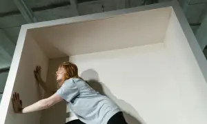 Eine Frau mit roten Haaren stemmt sich gegen eine Wand, als wolle sie die Opferrolle verlassen und aus einer Begrenzung ausbrechen.