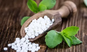 Süße Tabletten aus Stevia auf einem Holzlöffel, umgeben von grünen Blättern. Mögliche stevia nachteile sind hier nicht ersichtlich.