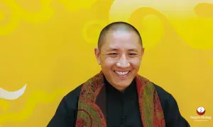 Ein Mann mit Glatze lächelt warm, trägt einen Schal und erklärt die Tummo Meditation.