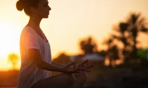 Frau in Meditation am Strand bei Sonnenuntergang, Gedanken loslassen.