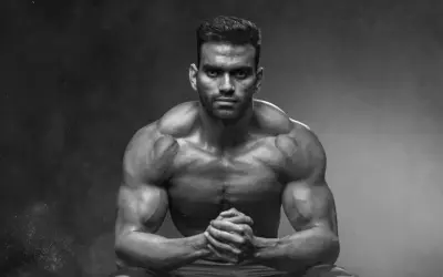 Muskulöser Mann mit ernstem Blick, Hände gefaltet. Die ecdysteron wirkung zeigt sich in seiner beeindruckenden Physis.