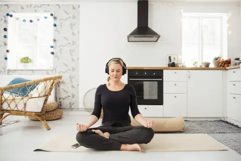 Frau meditiert mit Kopfhörern in einer Küche. Sie folgt einem 3-Minuten-Meditations-Text.
