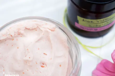 Cremige, rosafarbene Bodylotion mit Sheabutter in einem Glas. Daneben eine Flasche mit "Aloe Vera Bodylotion".