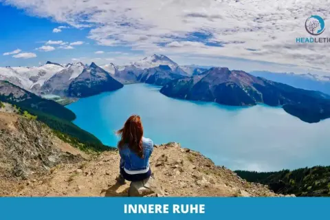 Frau meditiert gegen Angst und innere Unruhe auf einem Berg mit Blick auf einen türkisfarbenen See und schneebedeckte Gipfel.