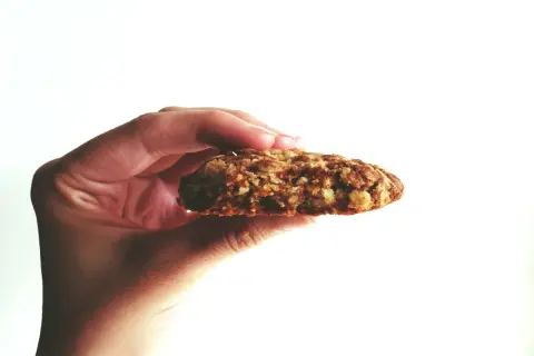 Hand hält ein Haferflocken-Keks. Warum keine Haferflocken bei Fructoseintoleranz? Haferflocken können bei Fructoseintoleranz Probleme bereiten.