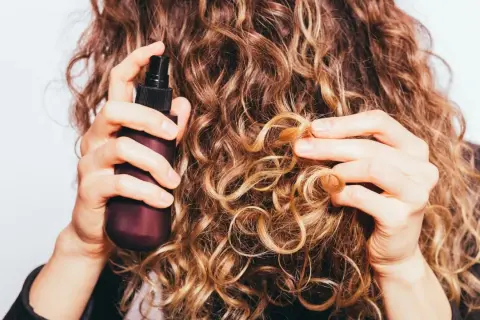 Frau sprüht mit einer Flasche auf ihre lockigen Haare. Perfekt für alle, die ihren eigenen Haarfestiger selber machen wollen.