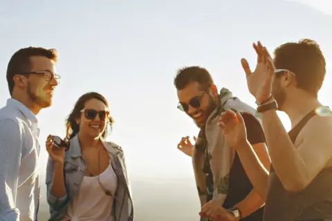 Vier Freunde lachen und tanzen ausgelassen in der Sonne. Sie zeigen, was sind echte freunde: Freude, Gemeinschaft und unbeschwerte Momente.