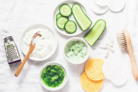 Zutaten für eine Gurkenmaske selber machen: Gurkenscheiben, Joghurt, geriebene Gurke, ein Hobel und weitere Utensilien.