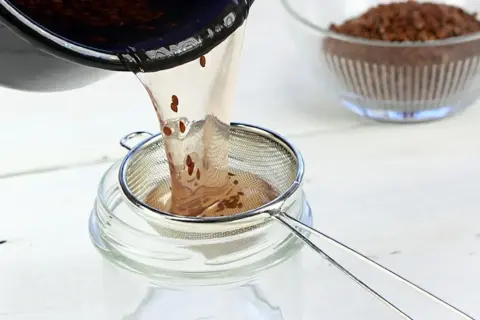 Flüssigkeit mit Leinsamen wird durch ein Sieb in ein Glas gegossen. Perfekt für leinsamen gesichtscreme selber machen.