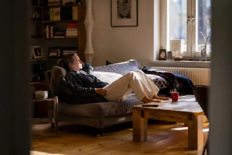 Frau entspannt sich auf dem Sofa, genießt das Sonnenlicht und praktiziert achtsame atem meditation.
