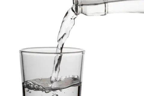Klares Wasser fließt aus einer Flasche in ein Glas. Die erfrischende birkenwasser wirkung wird durch die sprudelnden Bläschen im Glas angedeutet.