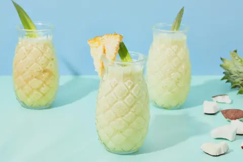 Erfrischende Kokoswasser Rezepte: cremige Drinks in Ananas-Gläsern, garniert mit Ananasblatt und Kokosstückchen.