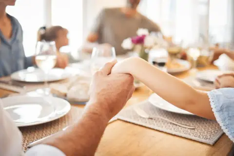 Familie hält Hände vor dem gemeinsamen Abendessen. Ein Moment des Gebets vor dem Essen.