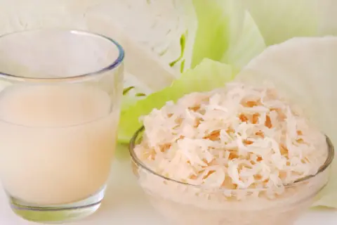 Ein Glas Sauerkrautsaft und eine Schüssel Sauerkraut, um die positive Sauerkrautsaft Wirkung Leber zu unterstützen.