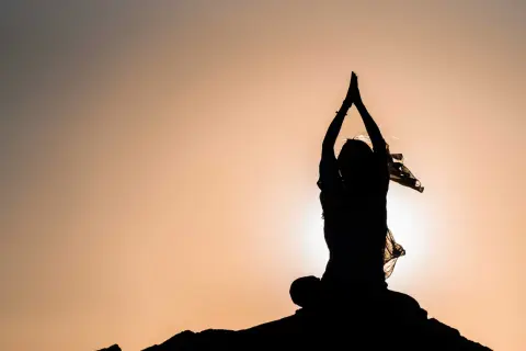 Silhouette einer Person in meditativer Haltung mit erhobenen Händen, die innere Freiheit verkörpert.