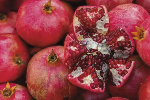 Ein aufgeschnittener Granatapfel mit vielen roten Kernen, umgeben von ganzen Früchten. Manche Menschen reagieren empfindlich auf Histamin, das auch im Granatapfel vorkommt.