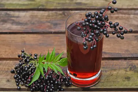 Ein Glas dunkler Holundersaft steht neben frischen Holunderbeeren. Die positive holunder wirkung psyche wird oft durch solche natürlichen Mittel unterstützt.
