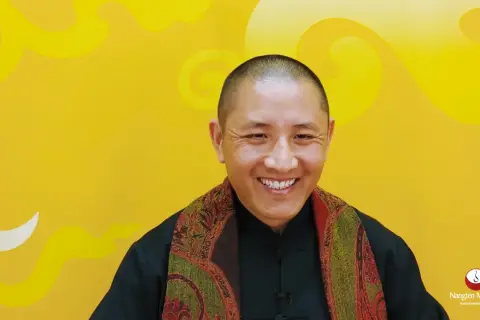 Ein Mann mit Glatze lächelt warm, trägt einen Schal und erklärt die Tummo Meditation.