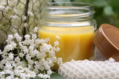 Ein Glas mit selbstgemachter Handcreme, umgeben von Holunderblüten und einem Stück Wabe.