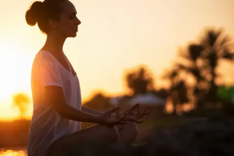 Frau in Meditation am Strand bei Sonnenuntergang, Gedanken loslassen.