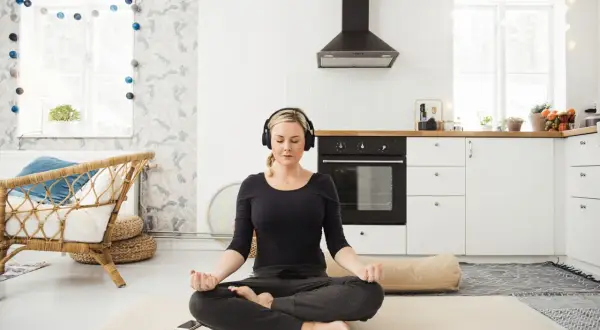Frau meditiert mit Kopfhörern in einer Küche. Sie folgt einem 3-Minuten-Meditations-Text.