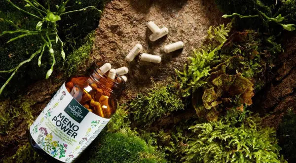 Braune Kapsel-Flasche mit "Meno Power" und Rotklee-Symbolen, umgeben von Moos und Steinen. Hilft bei der Bewältigung von Wechseljahrsbeschwerden, einschließlich möglicher Gewichtszunahme.