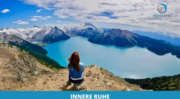 Frau meditiert gegen Angst und innere Unruhe auf einem Berg mit Blick auf einen türkisfarbenen See und schneebedeckte Gipfel.