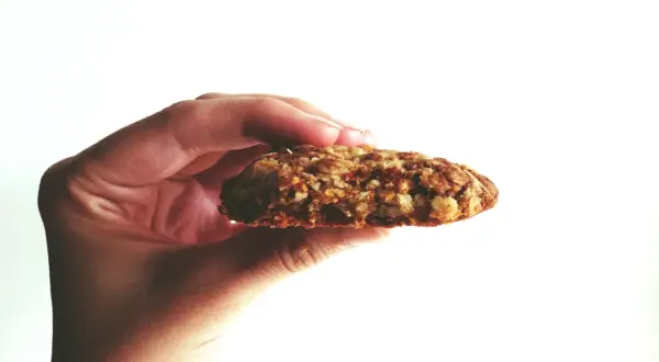 Hand hält ein Haferflocken-Keks. Warum keine Haferflocken bei Fructoseintoleranz? Haferflocken können bei Fructoseintoleranz Probleme bereiten.
