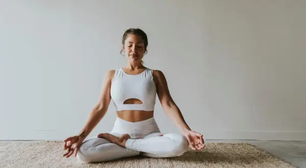 Frau in weißer Sportkleidung praktiziert Meditation. Ihre Augen sind geschlossen, Hände in Mudra-Position. Ein Bild, das Ruhe und Konzentration ausstrahlt, wie in vielen Meditation Studien.