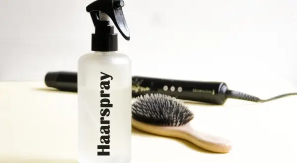 Flasche mit "Haarspray" Schriftzug, daneben Haarbürste und Glätteisen. Perfekt für haarspray selber machen.