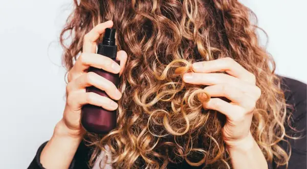 Frau sprüht mit einer Flasche auf ihre lockigen Haare. Perfekt für alle, die ihren eigenen Haarfestiger selber machen wollen.