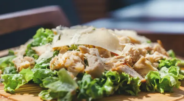 Frischer Romana Salat mit Hähnchenbrust und Parmesan, serviert auf einem Holzbrett.