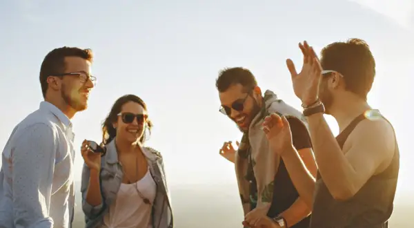 Vier Freunde lachen und tanzen ausgelassen in der Sonne. Sie zeigen, was sind echte freunde: Freude, Gemeinschaft und unbeschwerte Momente.